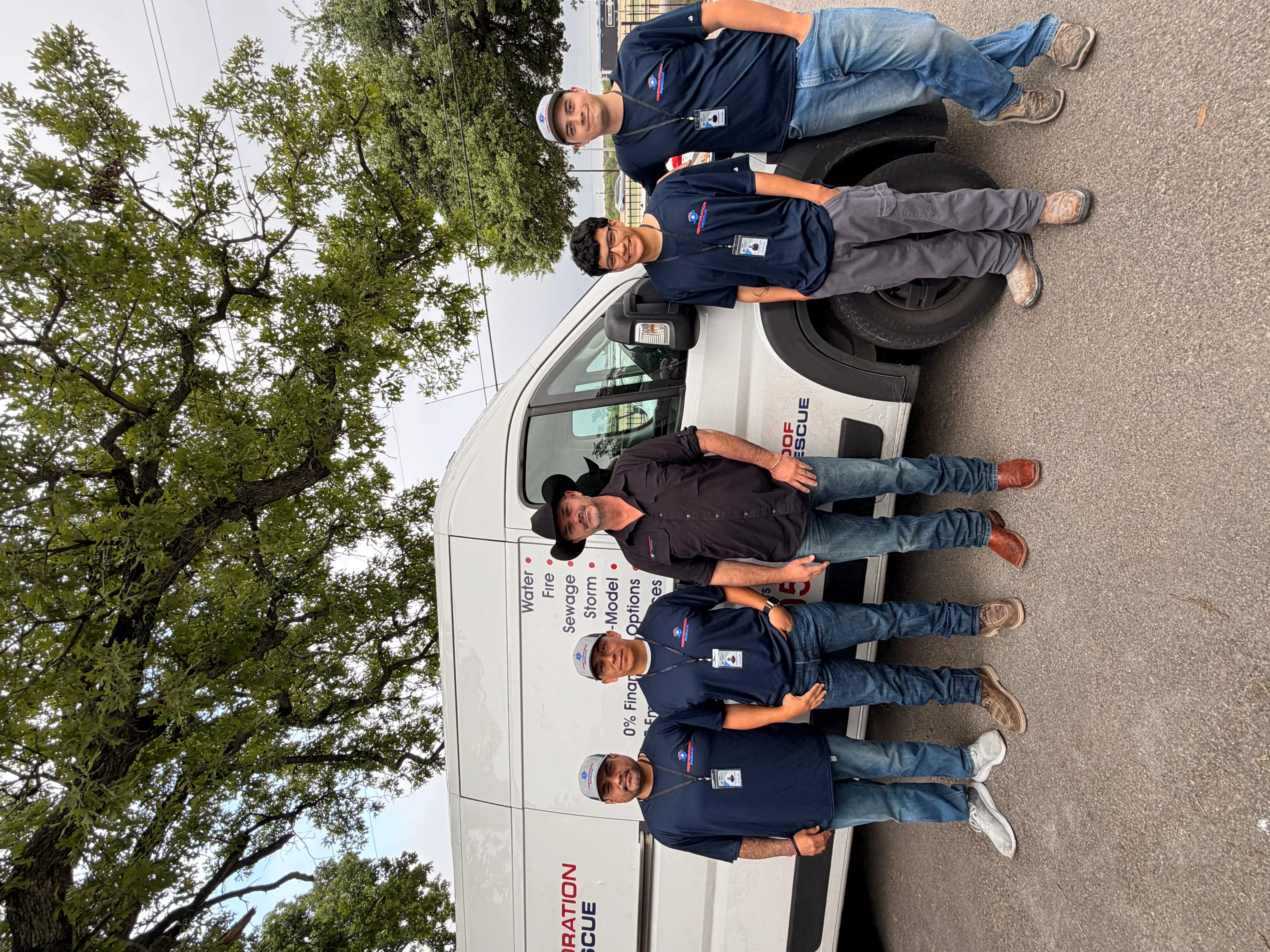 Water damage restoration team of five professionals in branded uniforms standing beside service vehicle