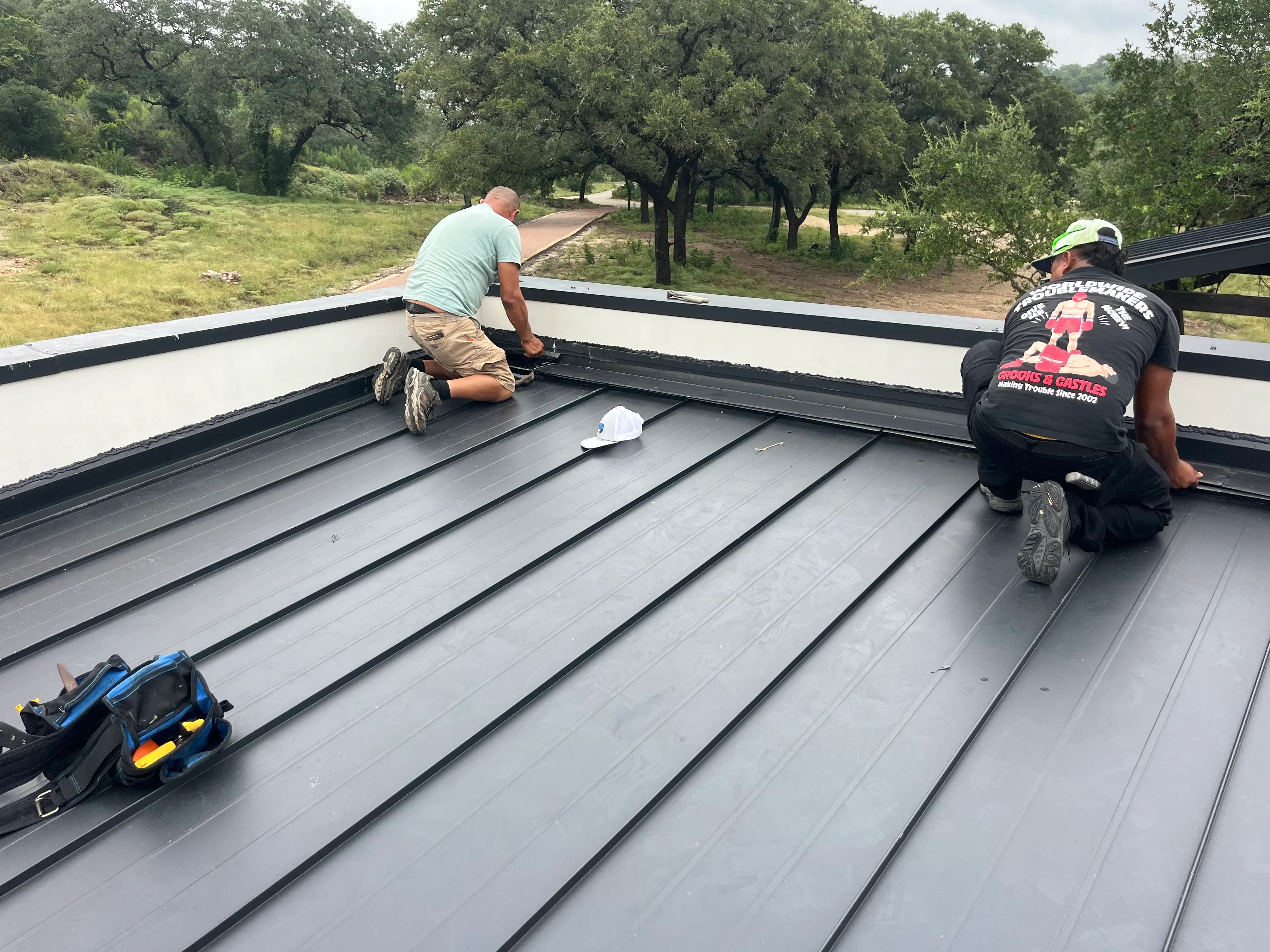 Two workers installing standing seam metal roof panels with white trim and black sealing