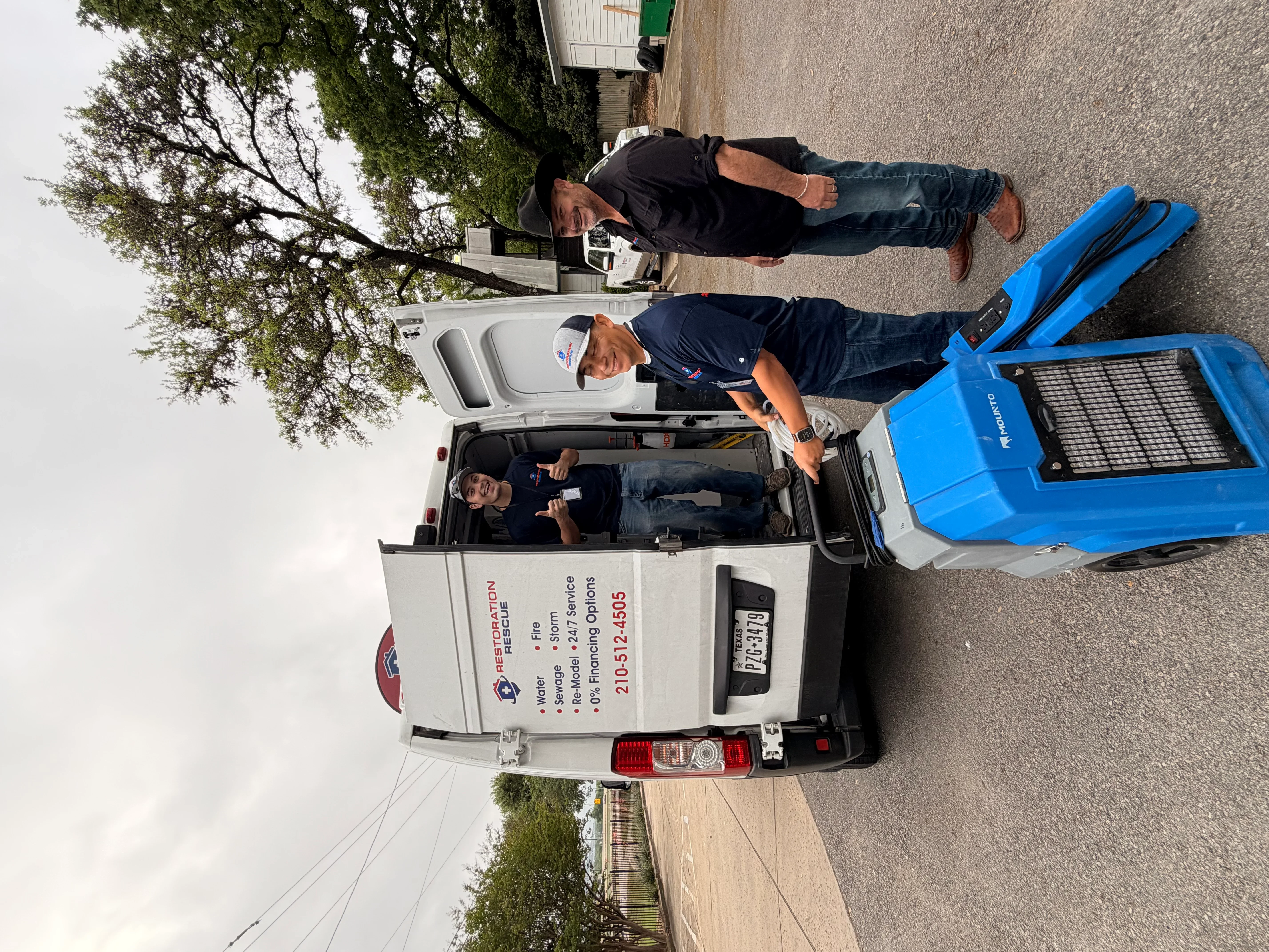 Water damage restoration team with extraction equipment and blue drying unit at residential site