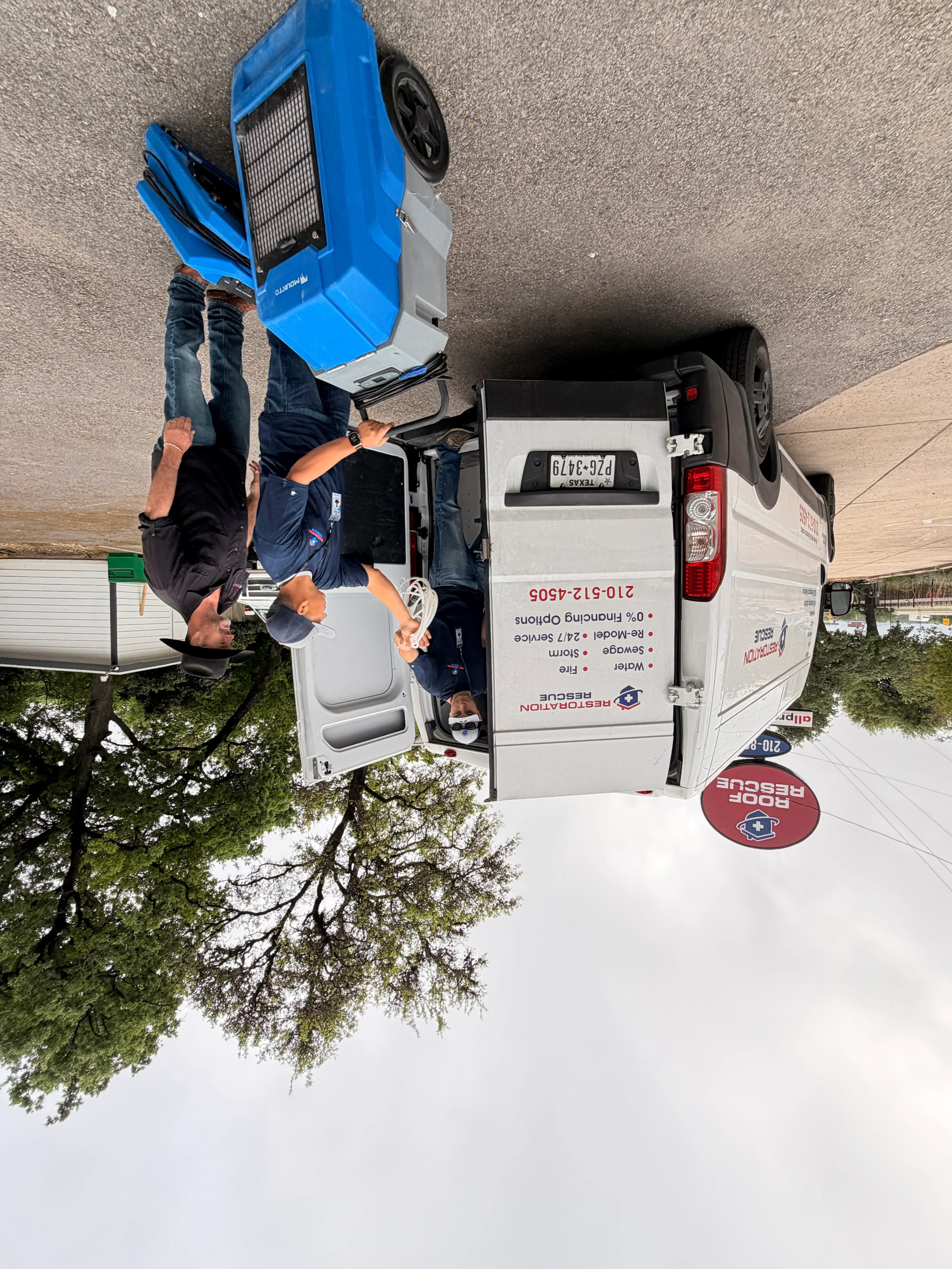 Water damage restoration crew with drying equipment and service vehicles on residential property